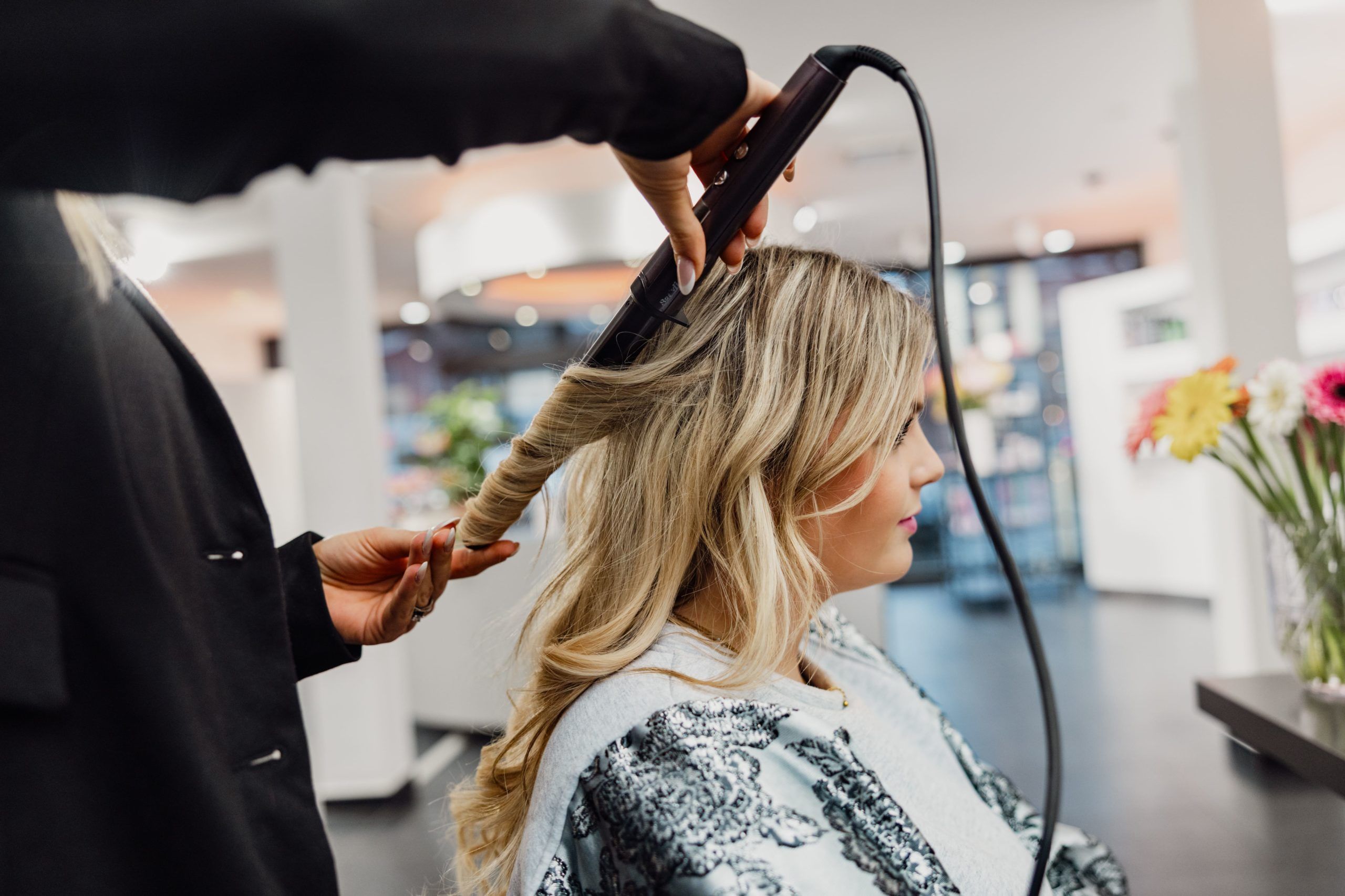 Kapster maakt zachte, glanzende waves in blond haar met een krultang in de salon van High Hair.